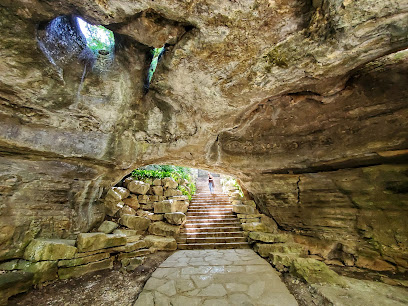 Cave entrance at Longhorn Cavern State Park showing a stone pathway leading to a stairway out, with a person standing near the exit.